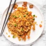 A plate of cauliflower fried rice with chopsticks resting on the side of the plate.