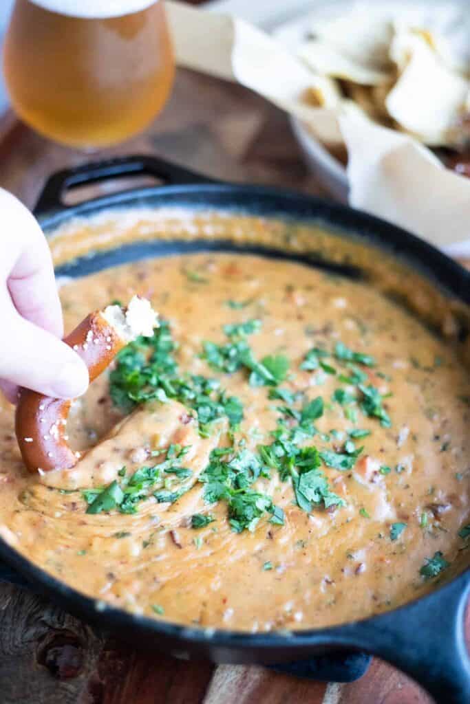 This is a picture of chipotle beer queso with a pretzel being dipped in.
