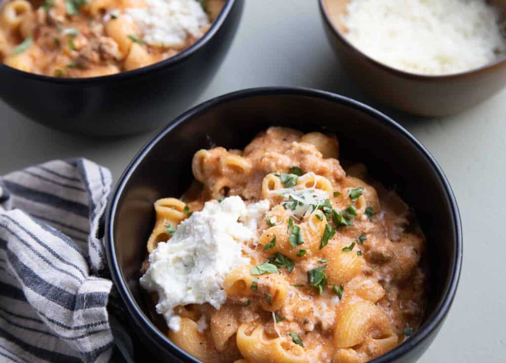 This is a picture of two bowls of lasagna soup with a bowl of parmesan on the side.