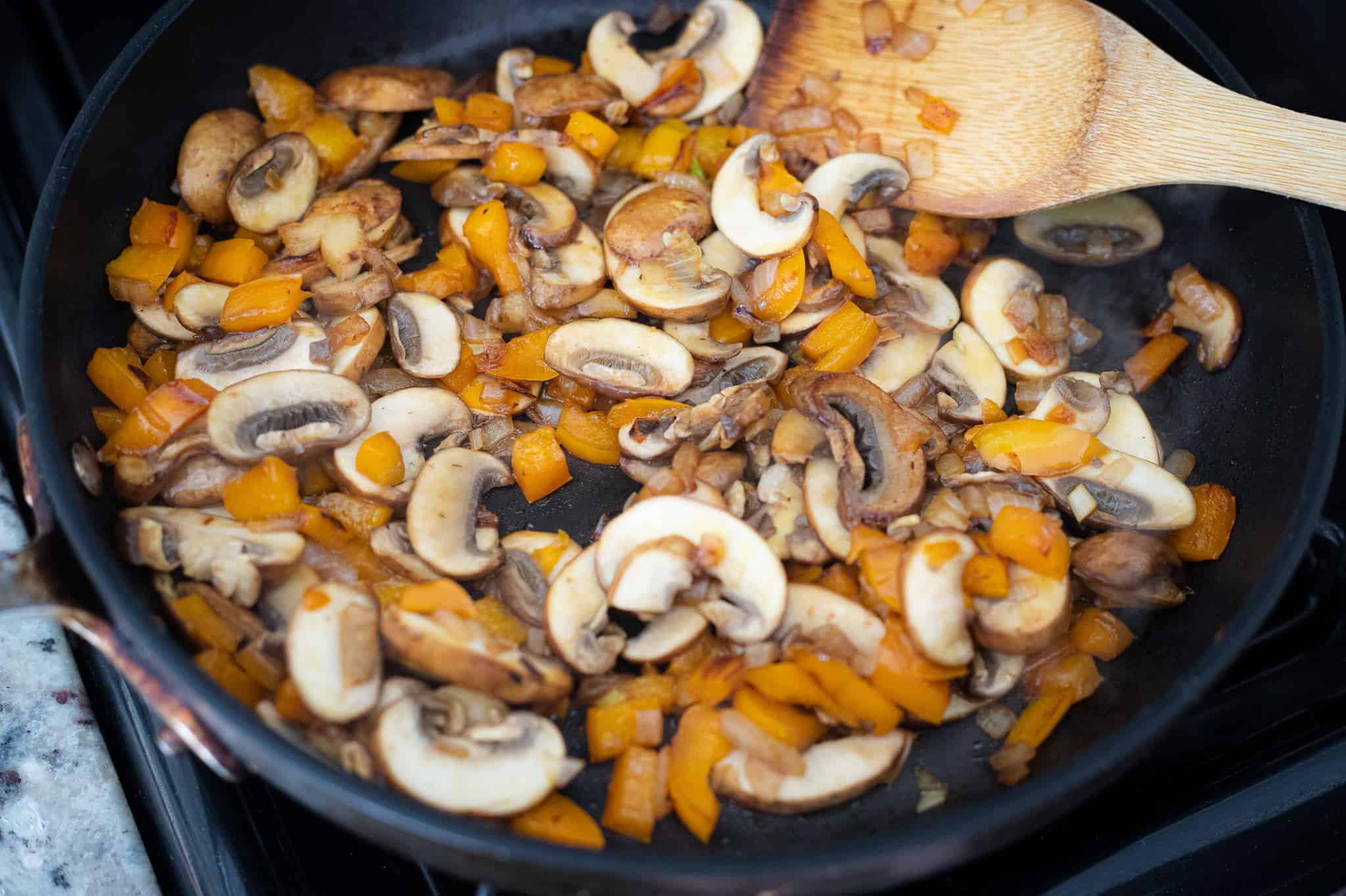Peppers and mushrooms cooking in a pan.
