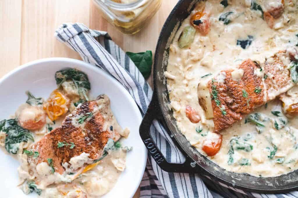 This is a picture of spinach and artichoke salmon on a plate and in a pan. 