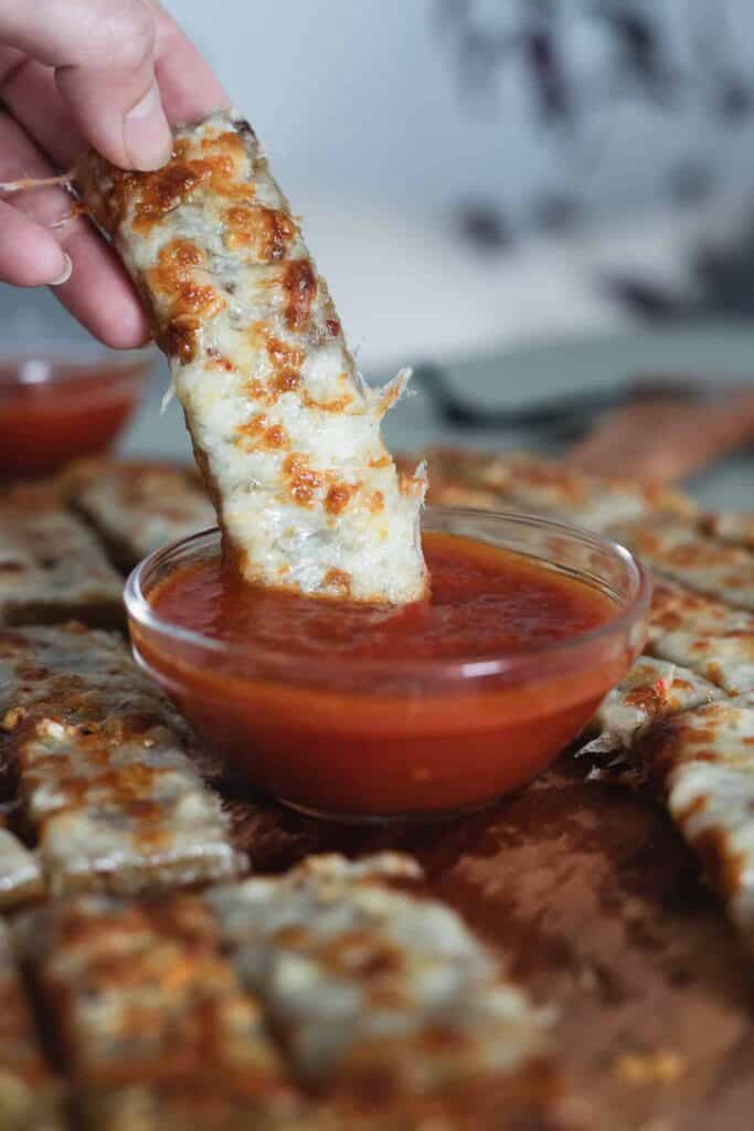 This is a picture of a cheesy breadstick being dipped into marinara sauce. The Hangry Economist.