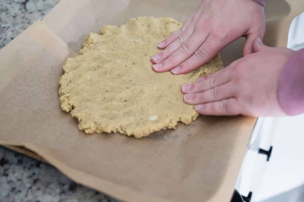 This is a picture of hands spreading dough on a sheet pan. The Hangry Economist.