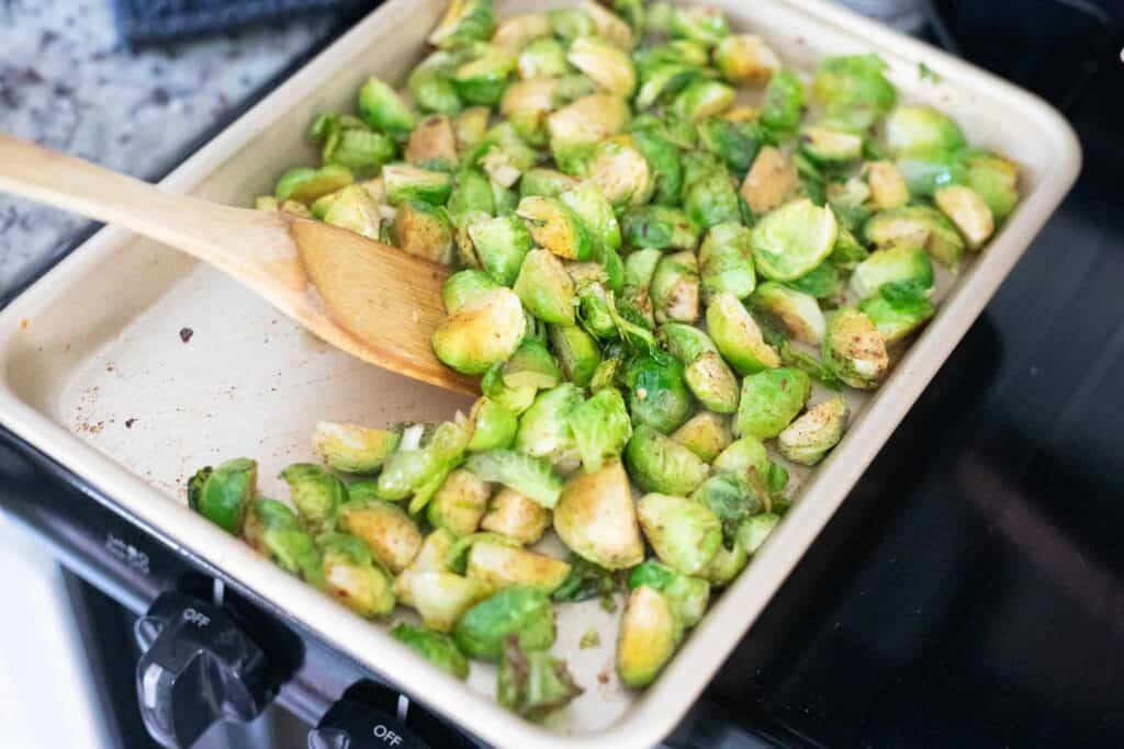 This is a picture of brussels sprouts on a pan being mixed with a wooden spatula. The Hangry Economist.