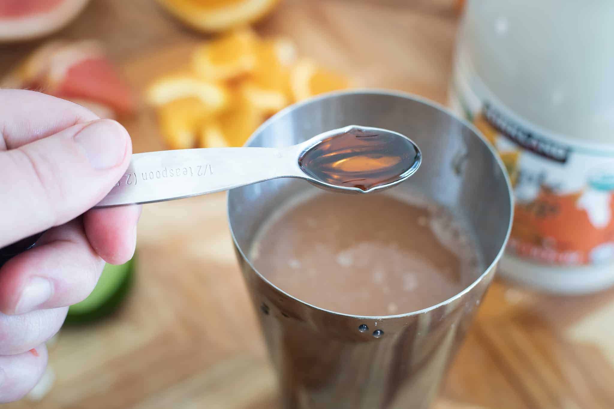 This is a picture of a measuring spoon with maple syrup being poured into a cocktail shaker. The Hangry Economist.
