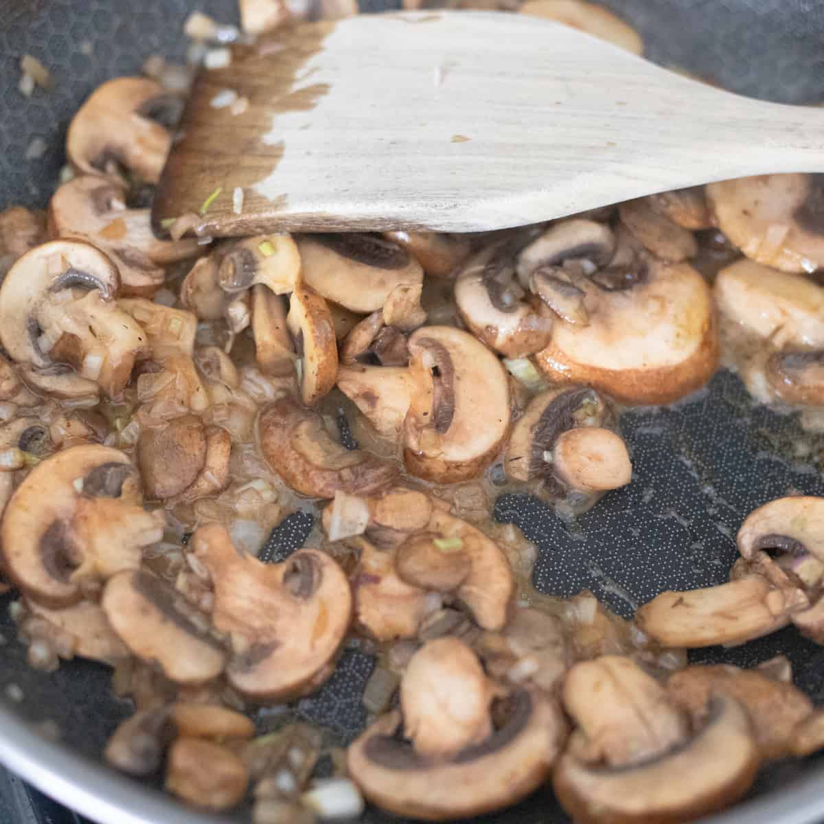 Shallots, mushrooms, and garlic cooking in a pan. 
