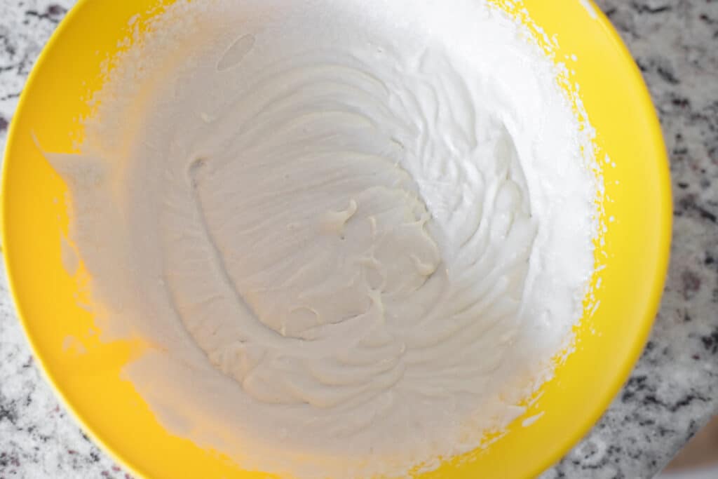 Whipped coconut cream with soft peaks in a yellow bowl. 