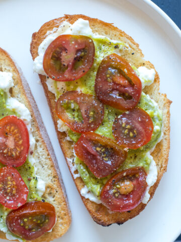 Two pieces of toast topped with cottage cheese, mashed avocado, and sliced tomatoes.