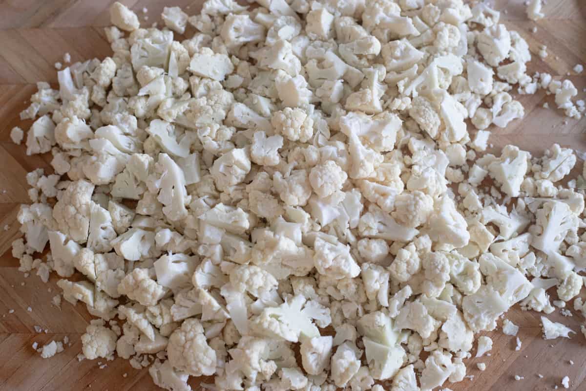 Medium-sized chunks of cut up cauliflower on a cutting board. 