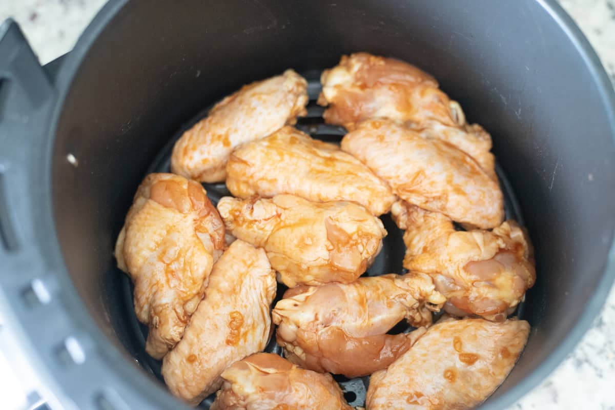 Raw chicken wings in an air fryer basket. 