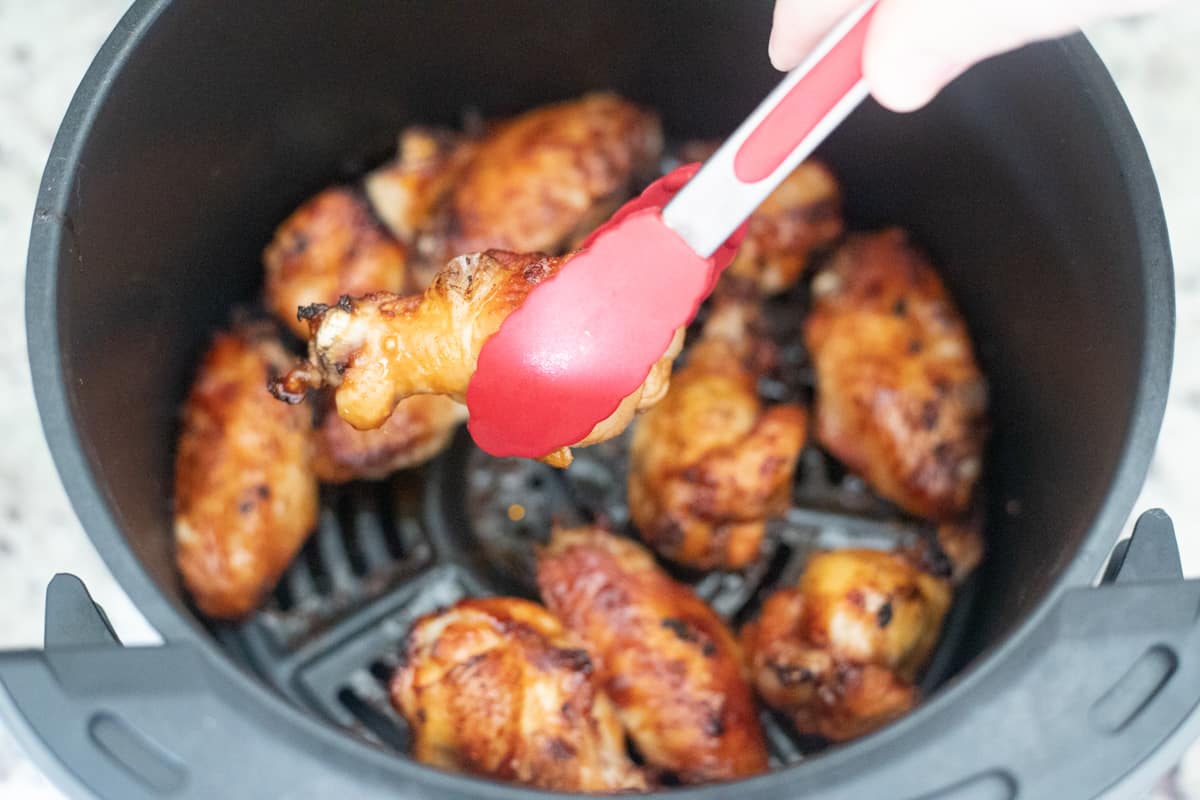 Cooked chicken wings in an air fryer being grabbed by tongs.