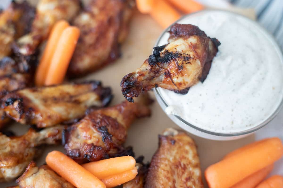 A marinated chicken wing being dipped into blue cheese dressing.