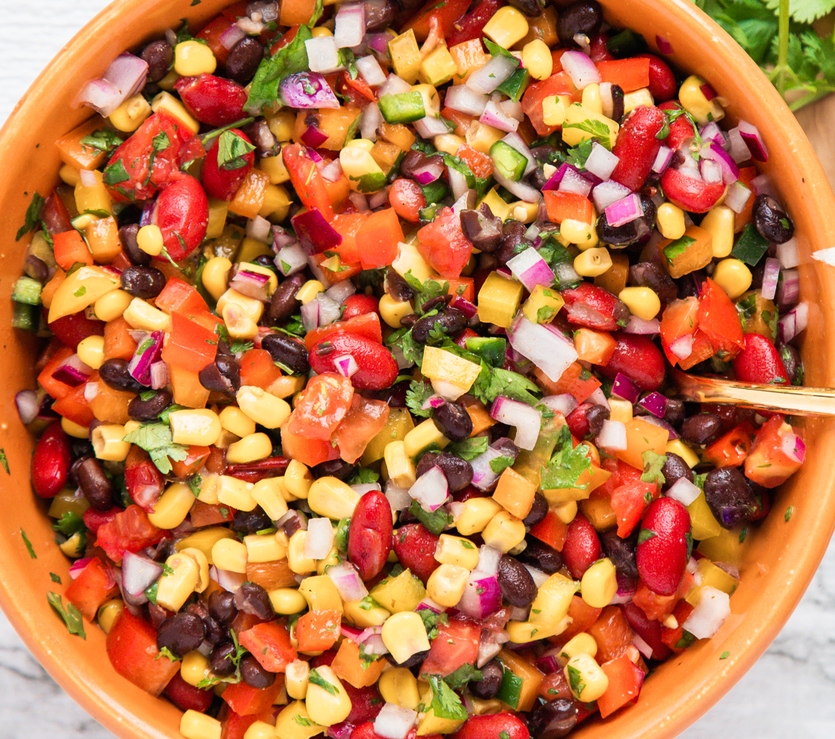 Close up of a large mixing bowl of corn, bean, and vegetable salsa. 