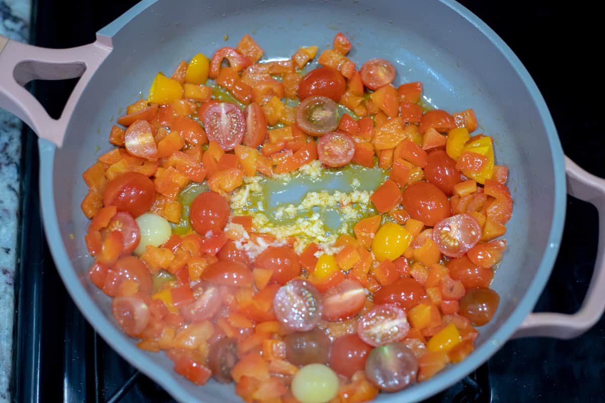 Tomatoes, red peppers, and garlic cooking in a pan. 
