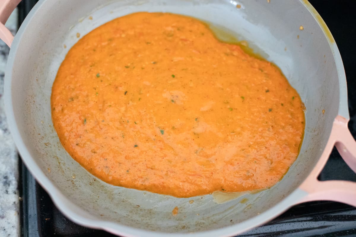 Red pepper, basil, and tomato sauce in a pan. 