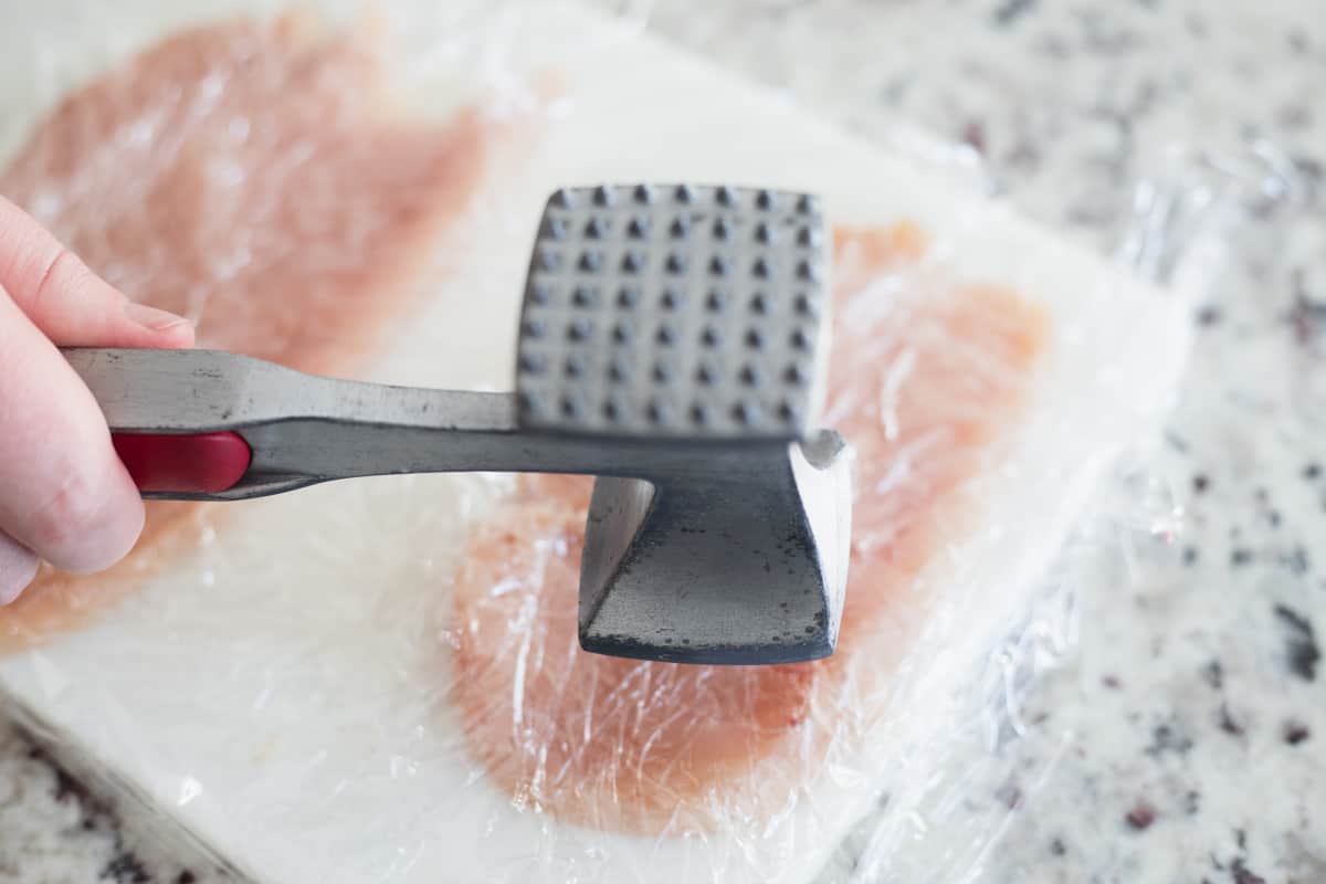 A meat tenderizer beating down a chicken breast that's covered in plastic wrap.