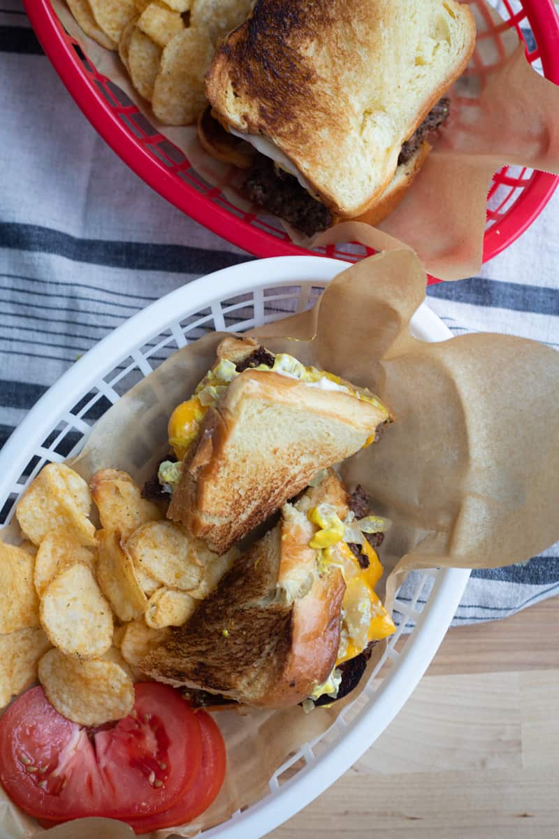 Two food baskets of grilled cheese burgers, chips, and tomato slices.