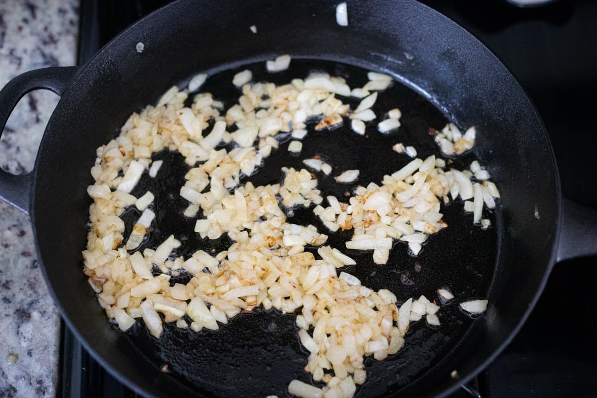 Diced onions cooking in a cast-iron pan. 
