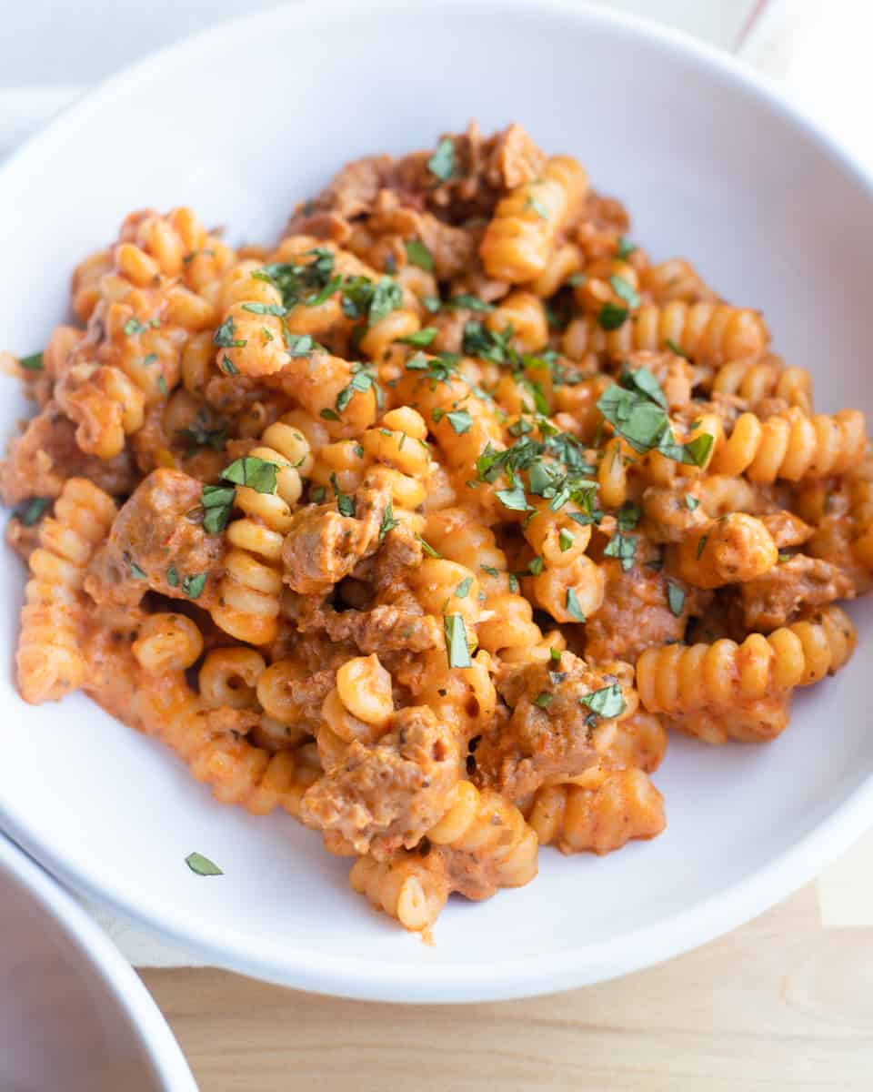 A bowl full of spicy Italian sausage pasta topped with basil. 