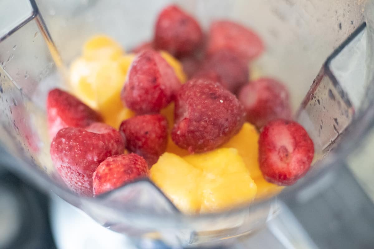 Frozen strawberries and mango chunks in a blender. 