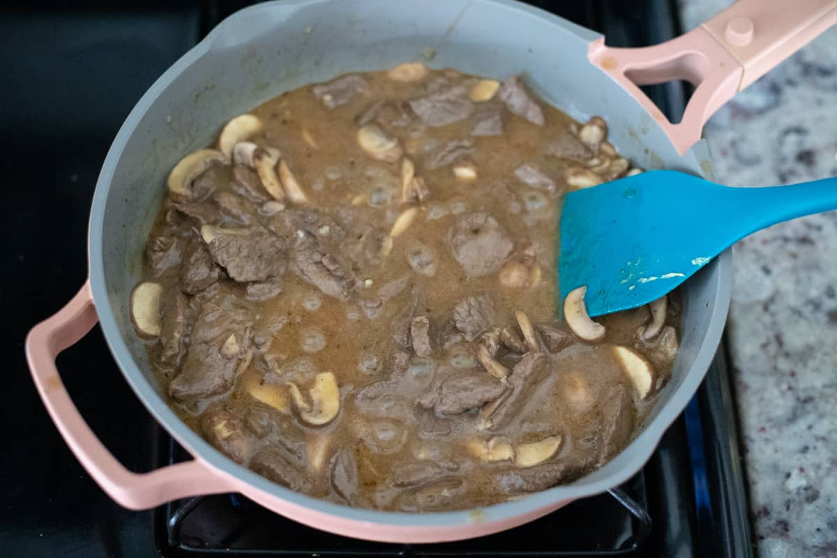 Mushrooms, steak, and a butter-based sauce cooking in a pan.
