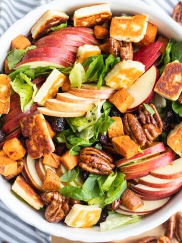 Fall harvest salad in a bowl with sweet potatoes, apples, pecans, lettuce, and halloumi cheese.