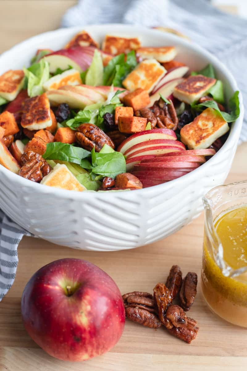 A bowl of fall harvest salad with an apple and dressing on the side. 