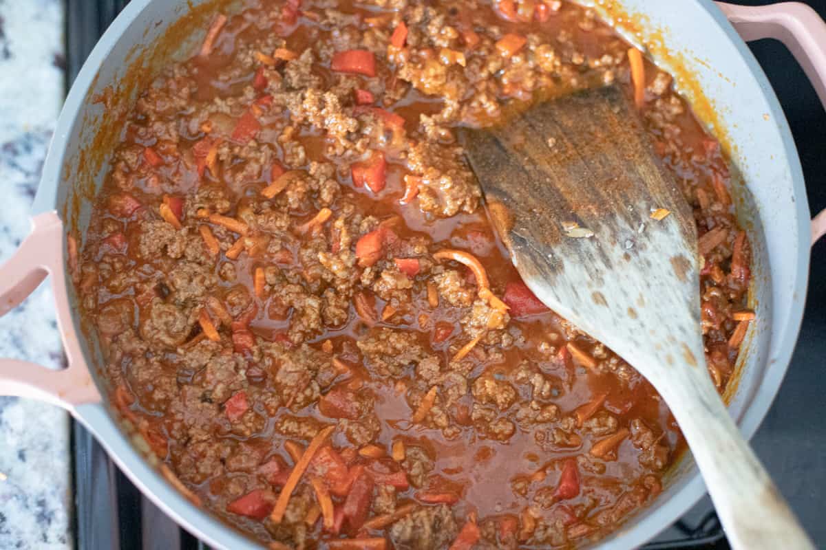 Ground beef and vegetables cooking in a boiling tomato-based sauce. 