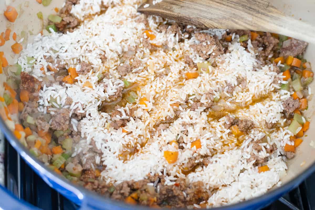 Rice, vegetables, and ground beef cooking in a pot with broth. 