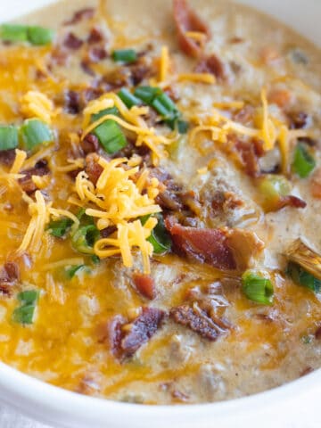 An up close view of a bowl of cheeseburger rice soup topped with shredded cheese, green onions, and crumbled bacon.
