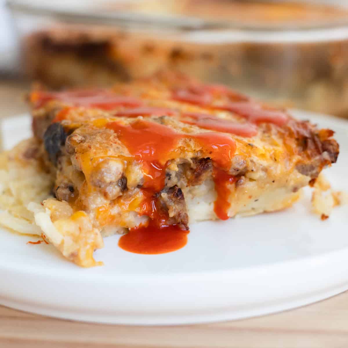 A piece of egg and sausage gravy breakfast casserole with hot sauce dripped on it.