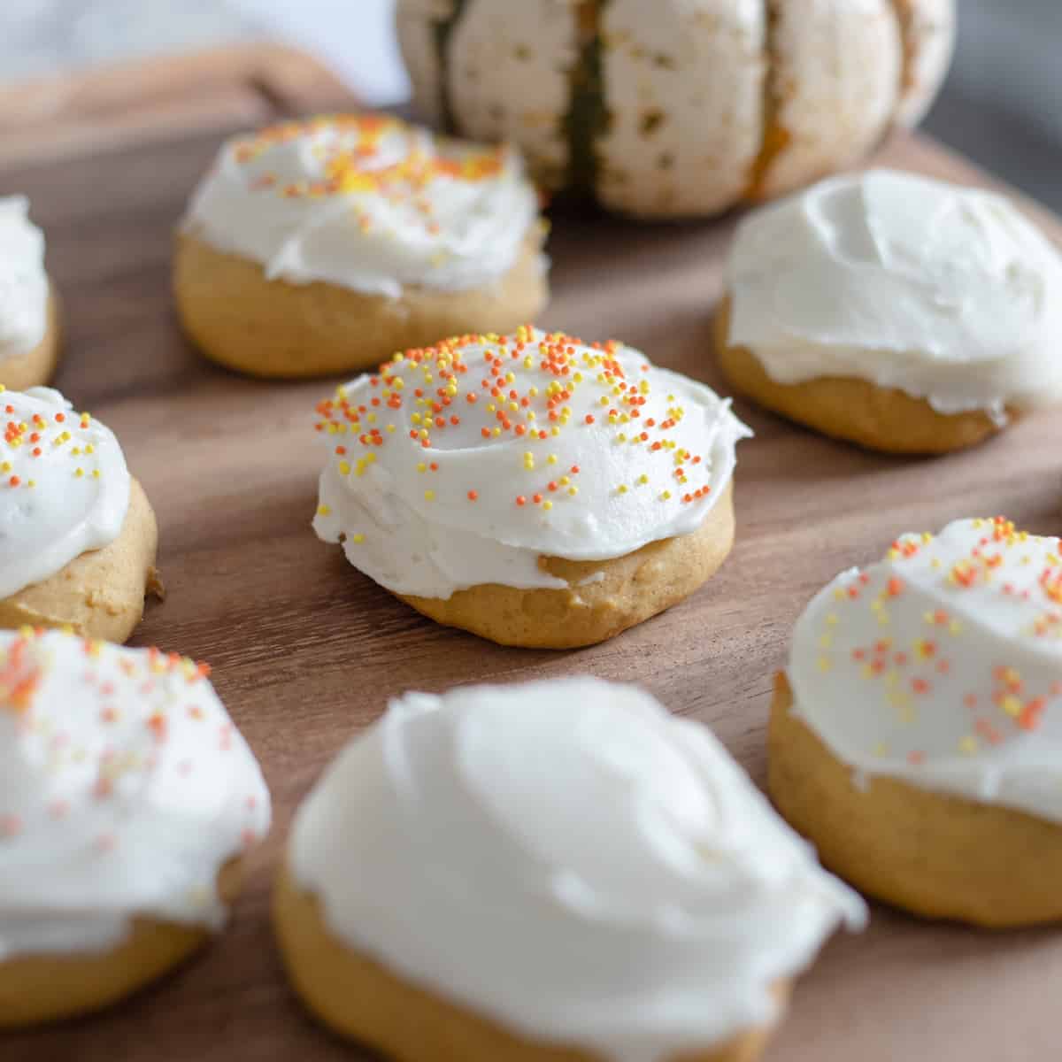 Frosted pumpkin cookies with sprinkles sitting on a cutting board.