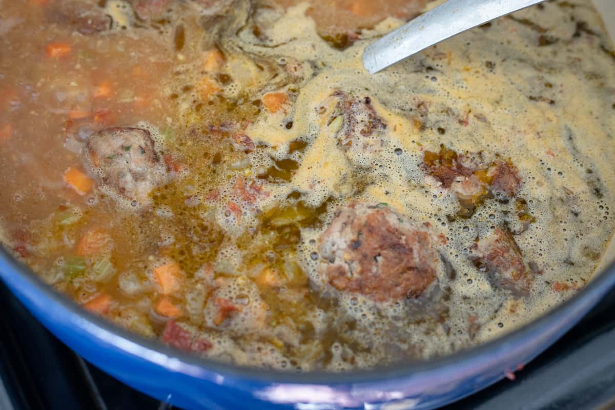 Meatballs, broth, and vegetables boiling in a dutch oven. 