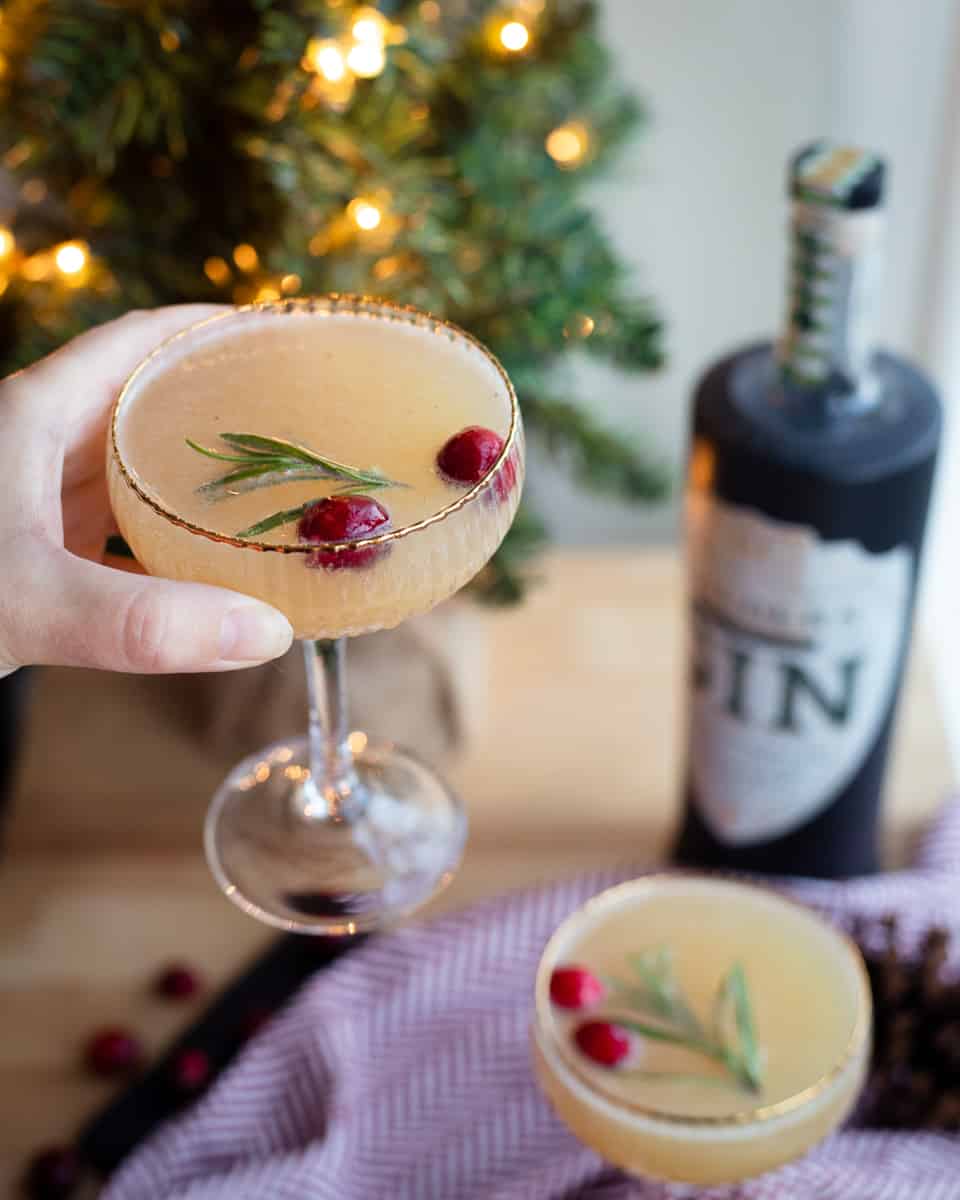 A glass of this cocktail being held up to a Christmas tree. 