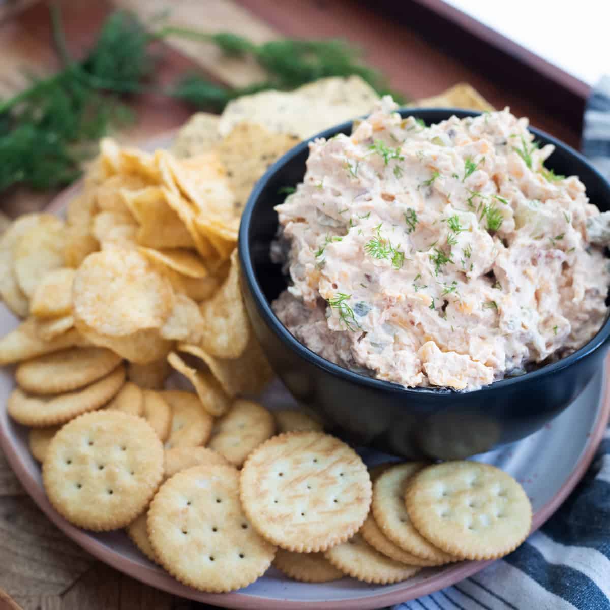 Pickle popper dip in a serving bowl surrounded by crackers and chips.
