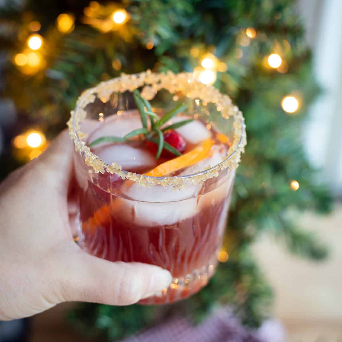 A pomegranate margarita being held in front of a Christmas tree. 