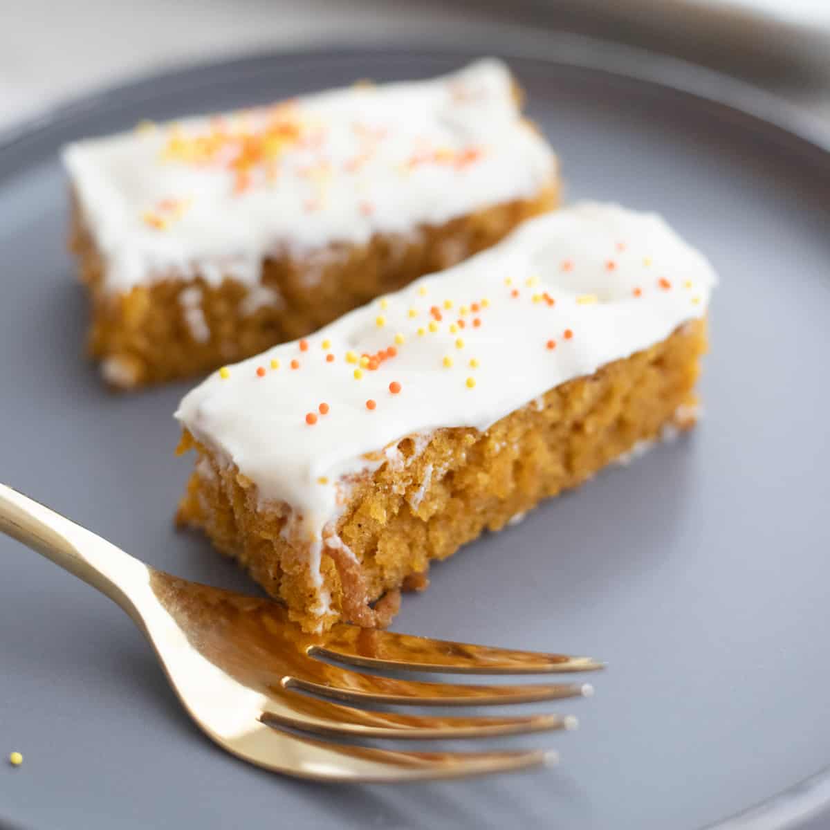 Two pumpkin cake bars on a plate with a fork. 