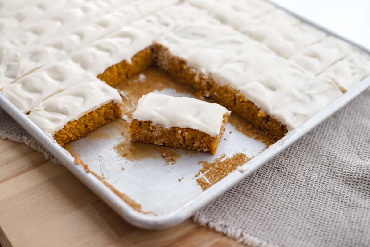 A pumpkin cake bar cut out of a sheet of pumpkin cake with cream cheese frosting. 