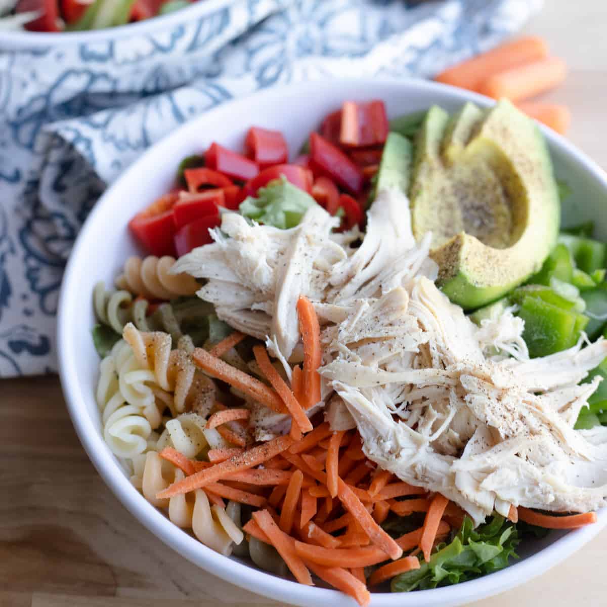 A bowl of rotisserie chicken garden salad with lettuce, carrots, chicken, avocado, bell pepper, and fusilli pasta. 