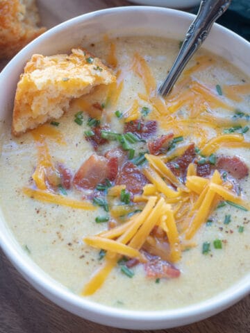 A bowl of cauliflower and baked potato soup topped with cheese, chives, and bacon.