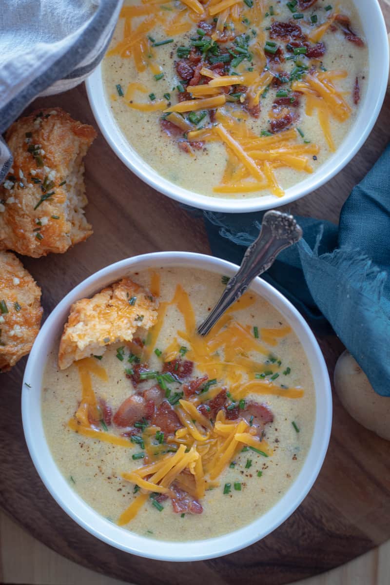 Two bowls of cauliflower and baked potato soup topped with cheese, bacon, and chives. 