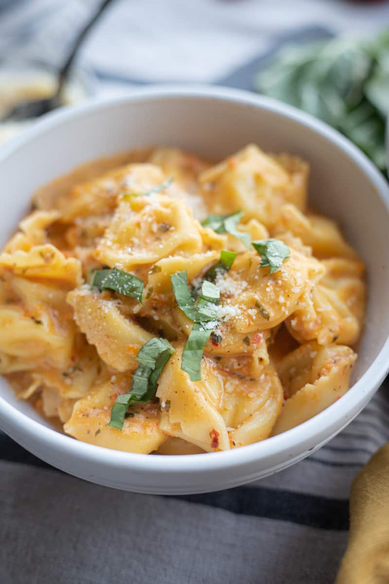 A bowl of roasted red pepper tortellini topped with basil and parmesan cheese. 