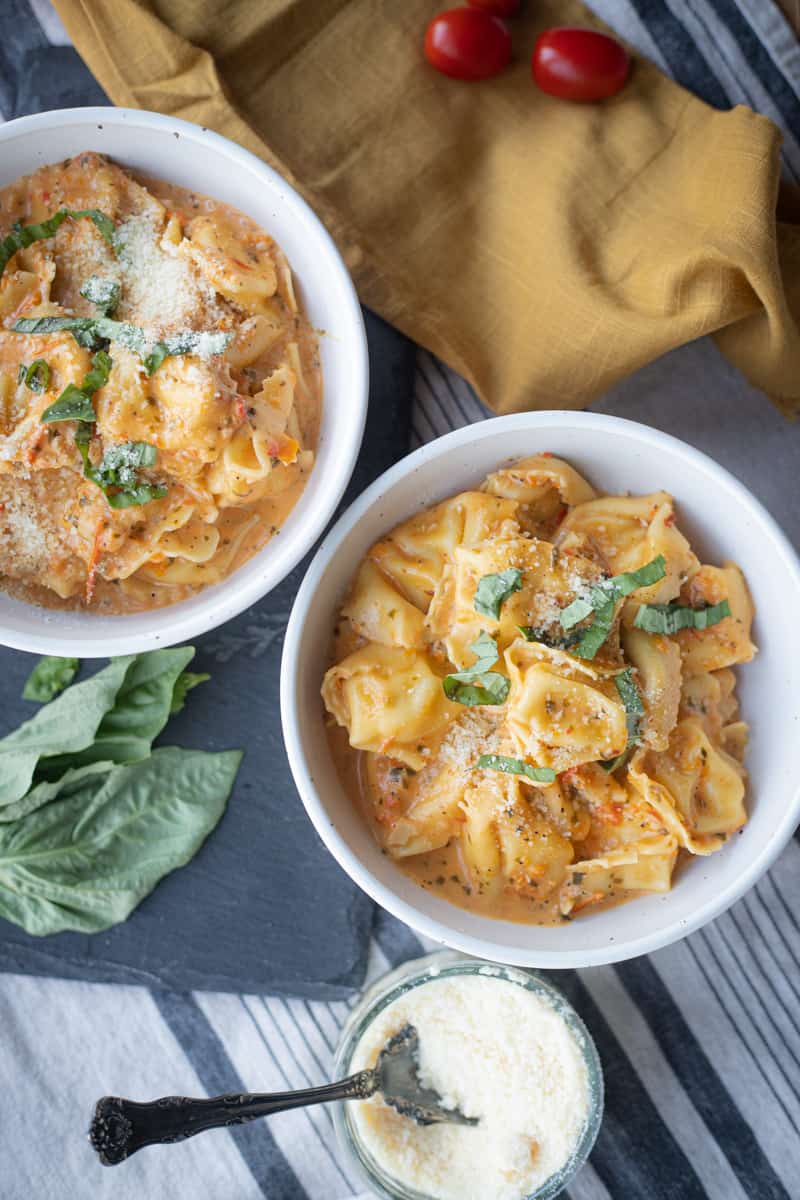 Two bowls full of roasted red pepper tortellini topped with parmesan cheese and basil. 