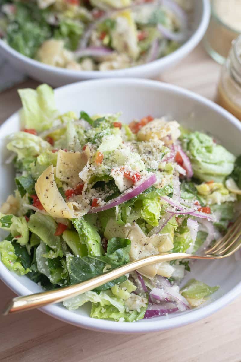 An italian salad with parmesan, onions, pimentos, artichokes, and lettuce in a bowl. 