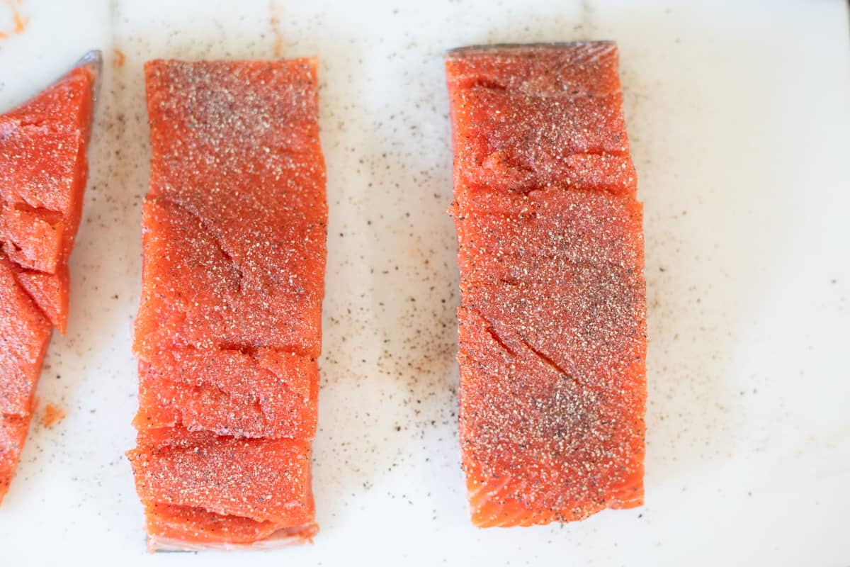 Salmon seasoned with salt and pepper on a cutting board. 