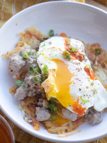 A bowl of hash browns, sausage gravy, and a runny egg.