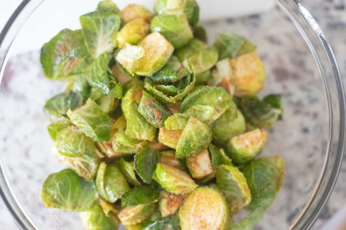 A mixing bowl with brussels sprouts, oil, and spices. 