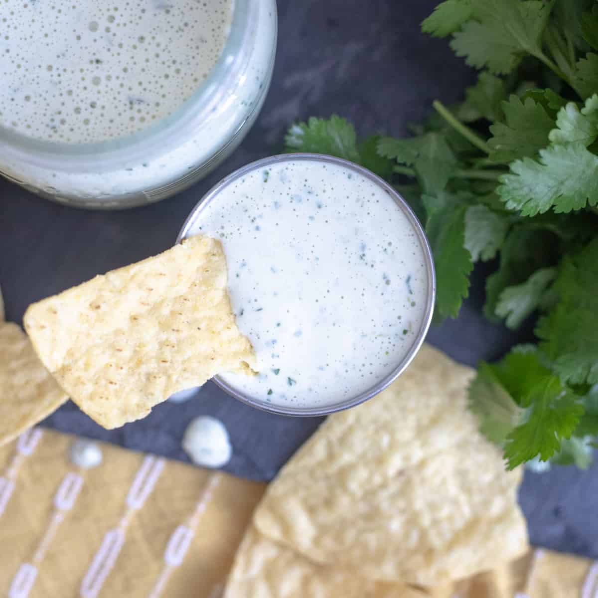 A serving bowl of cilantro lime sauce with a chip being dipped in it. 