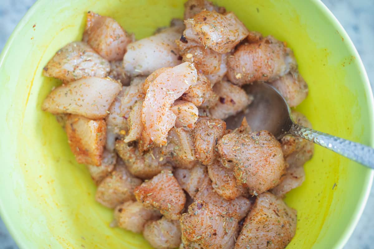 Seasoned raw chicken chunks in a mixing bowl. 