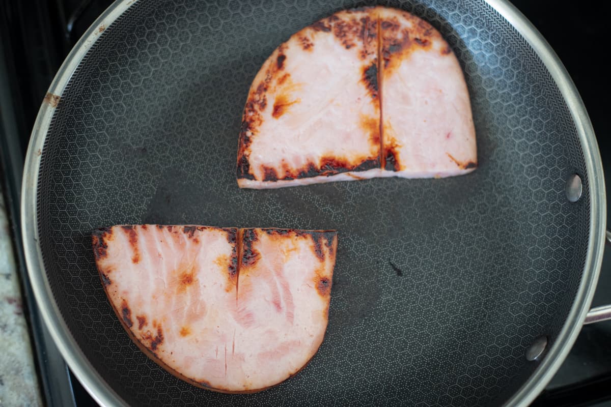 Ham steak cooking in a pan.